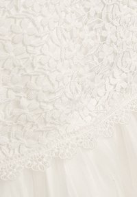 Weißes Kleid mit floraler Spitzenüberlagerung, das feine Stickereien und einen zarten, gewellten Rand aufweist. Weicher Tüllstoff unter der Spitze.