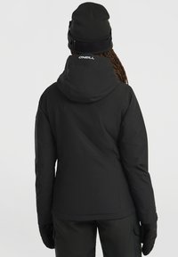 Zwarte geïsoleerde jas met een capuchon, voorzien van een gladde stof en een logo op de achterkant. Gepaarde met bijpassende zwarte handschoenen en broek.