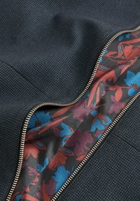 Ciemnoniebieska tkanina o fakturowanym wzorze, z podszewką w kwiatowy wzór w kolorach czerwonym, niebieskim i czarnym oraz ozdobnym złotym suwakiem.