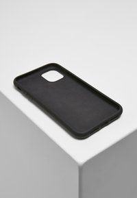 Coque de téléphone noire avec une finition mate, design slim, découpes précises pour les boutons et une texture lisse. Posée sur une surface blanche.