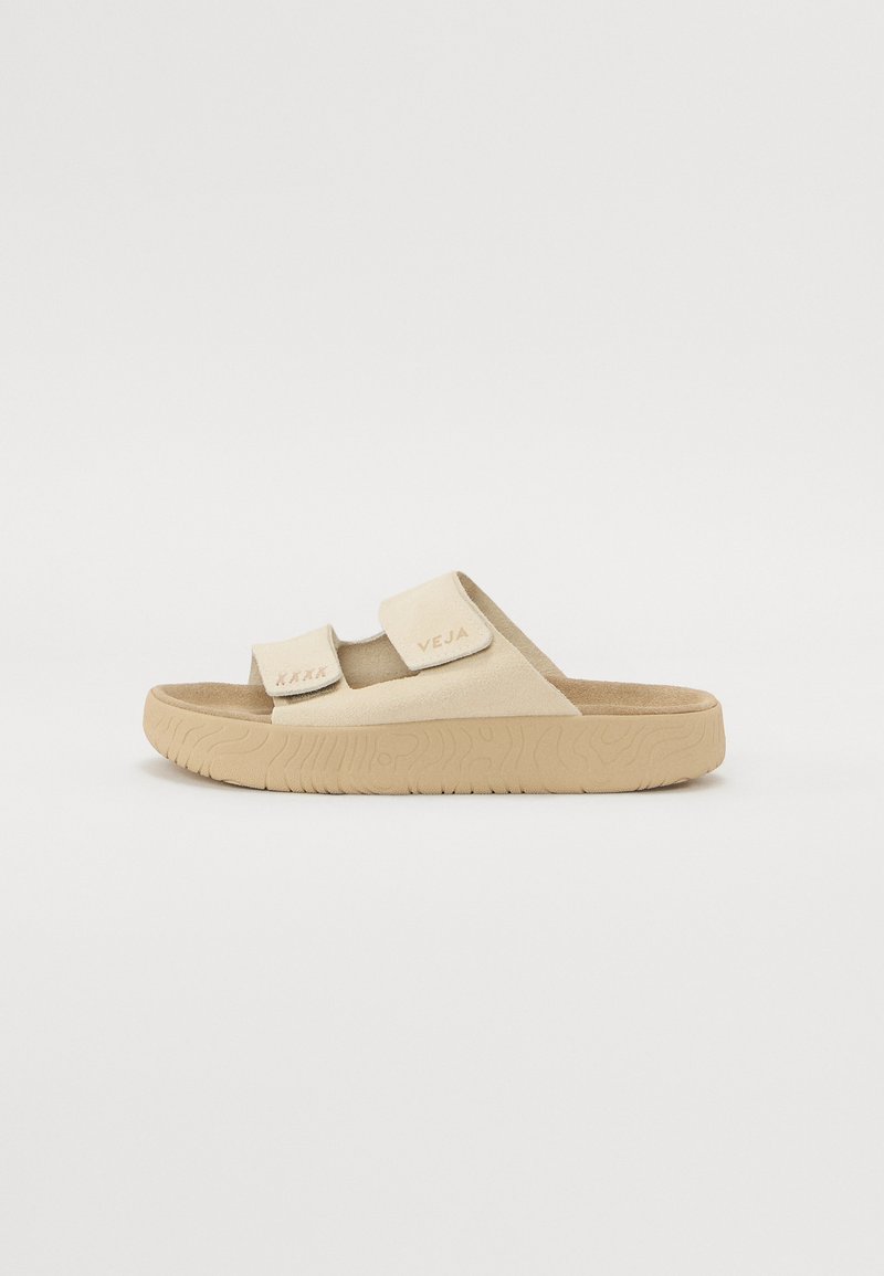 Beiga slide-sandaler med två justerbara remmar, texturerad ovandel och gummisula med ribbat mönster. Varumärkeslogotyp präglad på remmen.