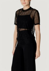 Camiseta de malla negra con un diseño en capas, que presenta mangas cortas y un patrón de logo de A/X, combinada con pantalones negros ajustados.
