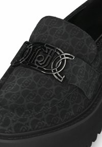 Schwarze Wildleder-Loafer mit strukturiertem Muster, ausgestattet mit einer glänzenden schwarzen Logo-Schnalle und einer dicken, gemusterten Gummisohle.