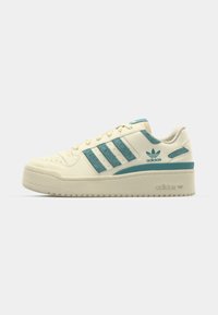 Tenisice krem boje s tirkiznim naglascima, s tri strukturirane pruge, gumenim potplatom i podstavljenim ovratnikom. Oznaka s Adidas logom.