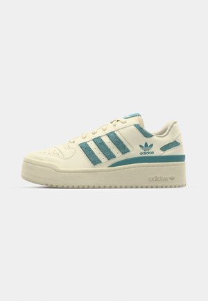 Krémové tenisky s tyrkysovými akcenty, mají tři texturované pruhy, gumovou podrážku a polstrovaný límec. Označeno logem Adidas.
