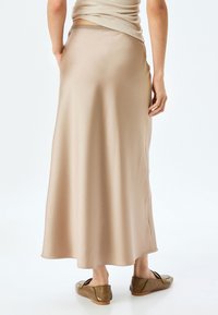Beige satin maxi nederdel med en glat tekstur, sidedel og et blødt, flydende design. Parret med brune, strukturerede flade sko.