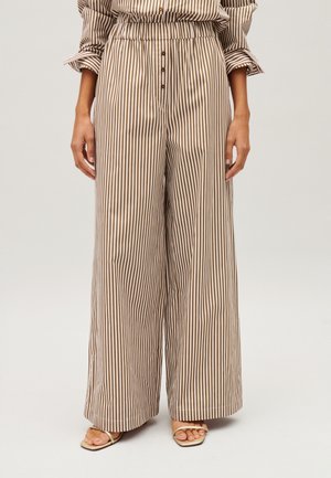 Beige en bruine wijde broek met verticale strepen en knopen in de taille, gedragen met beige sandalen met open teen.