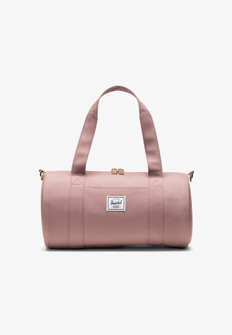 Pink cylindrical duffel bag with dual shoulder straps, gold zipper, and white Herschel brand logo patch on front center.
