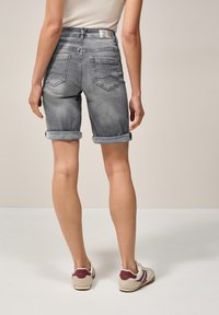 Pantalones cortos de mezclilla gris con dobladillos enrollados, que cuentan con bolsillos traseros y un pequeño parche con el logo en la cinturilla. Textura suave con un ligero desgastado.