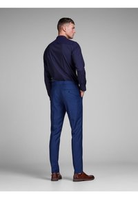 Navy button-up shirt paired with tailored blue trousers. Trousers feature a back pocket; brown shoes accent the outfit. Textured fabric.