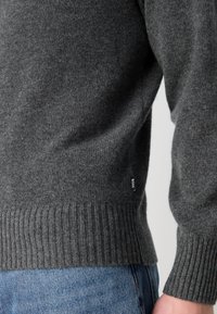 Maglione grigio a maglia con orlo e polsini a costine; presenta una piccola etichetta nera "BOSS" sul lato. Tessuto morbido, design contemporaneo.