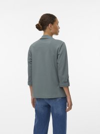 Šedá, volně střižená bunda s límcem a ohrnutými rukávy, vyrobená z měkkého materiálu. Zadní strana má čistý design bez ozdob.