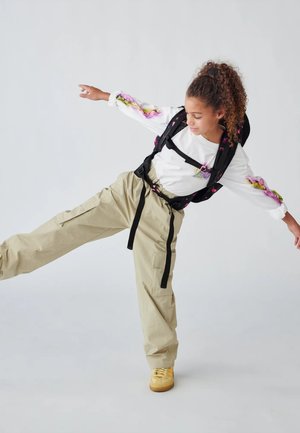 Black backpack with floral accents, white long-sleeve shirt with pink and green details, beige cargo pants, and yellow sneakers.