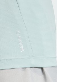 Gaiši zils sporta krekls ar teksturētu audumu, uz kura baltā krāsā redzams Climacool logo. Vienkāršs dizains, īsas piedurknes un gludas šuves.