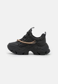Black sneaker made of leather with a chunky sole, featuring a gold chain detail across the upper. Textured finish and rounded shape.