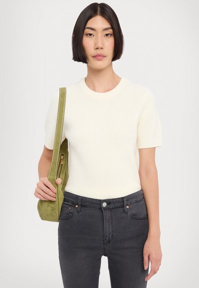 Pulover alb cu dungi, cu maneci scurte și guler rotund, asortat cu blugi închiși la culoare și o geantă de umăr verde din suede cu fermoar.
