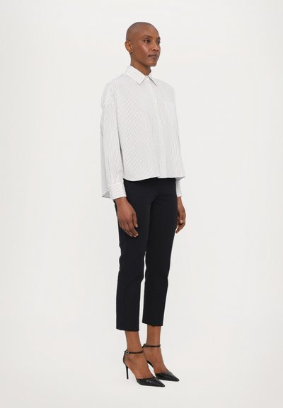 Wit en marineblauwe gestreepte cropped shirt met een kraag, gedragen met strakke zwarte broeken en zwarte puntige hakken. Gladde stoffen textuur.