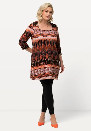 Túnica con estampado y escote cuadrado, en colores naranja, negro y rosa. Combinada con leggins negros y tacones naranjas.