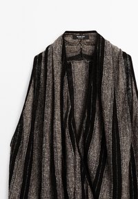 Cardigan ouvert à rayures grises et noires avec une texture en maille lâche et un col châle, suspendu sur un fond blanc.