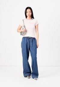 Rosa bomullströja med tryck "Los Angeles", i kombination med lösa blå denimbyxor och silverfärgade högklackade skor. Tillbehören inkluderar en grå handväska.