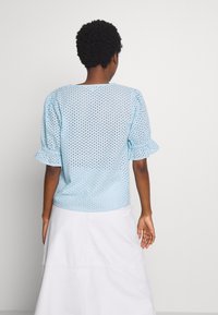 Jasnoniebieska bluzka na krótki rękaw z teksturowanej tkaniny z małymi otworami. Rękawy z falbanami dodają szczegółu, a luźny krój i okrągły dekolt zapewniają komfort.
