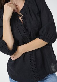 Blusa nera in lino con maniche a palloncino a tre quarti, dotata di scollatura con lacci e delicati dettagli ricamati lungo il pattina anteriore.