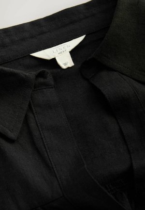Schwarzes Leinenhemd mit klassischem Kragen, Druckknopf-Leiste und subtiler Textur, versehen mit einem Etikett zur Materialzusammensetzung.