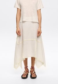 Linen blend dress in cream, featuring scalloped hem, yellow floral accents, and a layered skirt. Paired with black sandals and red straps.