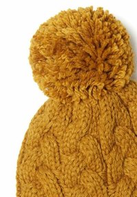 Hořčicově žlutý pletený beanie má strukturovaný kabelkový vzor a velký, načechraný pom-pom nahoře. Vyrobeno z měkké příze.