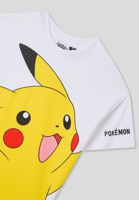 T-shirt bianca a maniche corte con una grande grafica di un personaggio Pokémon giallo, con guance rosse e dettagli neri. "Pokémon" stampato sulla manica.