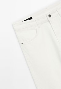 Jeans in denim bianco con una vestibilità slim, caratterizzati da un piccolo rivetto nero sulla tasca anteriore e un'etichetta nera all'interno della cintura.