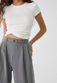 T-shirt blanc à manches courtes côtelé associé à un pantalon gris taille haute avec une taille ceinturée et des détails plissés.