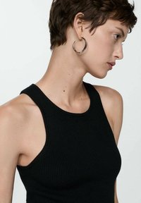 Débardeur noir à côtes avec un col haut et de larges bretelles. Le modèle porte une boucle d'oreille en argent. Texture lisse et design ajusté.