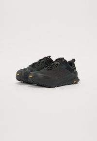 Czarne buty do biegania w terenie z teksturowaną powierzchnią, wzmocnionym piętą i gumową podeszwą. Posiadają czarne sznurowadła oraz pomarańczowe logo Vibram po boku.