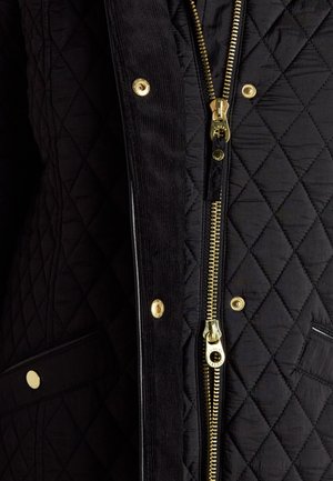 Veste matelassée noire avec fermeture éclair dorée et boutons-pression, avec un rabat en velours côtelé et une poche visible avec bouton doré.
