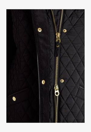 Schwarze gesteppte Jacke mit goldfarbenem Reißverschluss und Druckknöpfen, mit einem Kordstoff-Lappen und sichtbarer Tasche mit goldfarbigem Knopf.