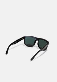 Ochelari de soare negri cu lentile de culoare verde închis. Ramele au un finisaj mat, o formă ușor rotunjită și brațe curbe cu un detaliu de balama.