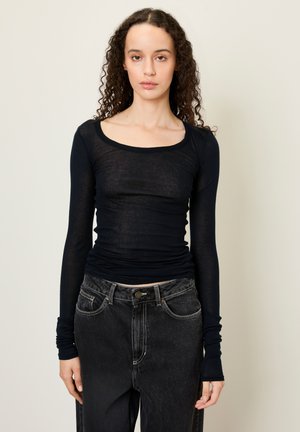 Haut noir à manches longues en tissu léger et transparent avec un col arrondi, une coupe ajustée et des manches cintrées, associé à un jean foncé taille haute.