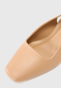 Chaussure plate beige avec un bout carré et une bride arrière, en cuir lisse.