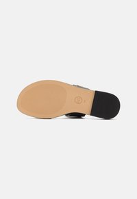 Semelle de sandale avec avant marron clair, talon noir, grip texturé et logo circulaire indiquant la taille 7M sur fond blanc.