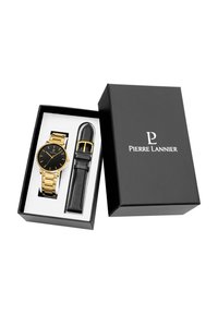 Reloj de metal dorado con esfera negra, alojado en una caja negra con interior plateado. Incluye una correa de cuero negra y hebilla dorada.