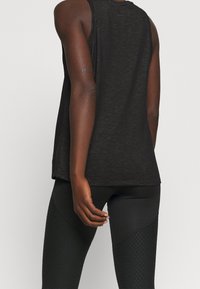 Černý bezrukávový top vyrobený z lehké tkaniny, s volným střihem. Zadní strana je hladká s oblým lemem, doplněný o texturované černé legíny.