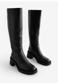Bottines en cuir noir jusqu'au genou avec un talon épais et une semelle texturée. Équipées d'une fermeture éclair latérale et d'une finition lisse. Détails cousus le long des coutures.