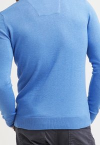 Pull bleu clair en tricot doux, avec des manches longues, un col rond, et des poignets et un ourlet côtelés avec une texture subtile.
