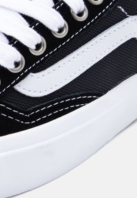 Μαύρο υφασμάτινο αθλητικό παπούτσι με λευκή δερμάτινη πλαϊνή ρίγα, με λευκά κορδόνια, ασημένιες τρύπες κορδονιών και λευκό ραφές σε υφασμένο επάνω μέρος.