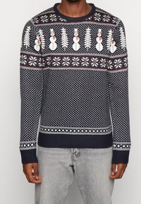 Maglione lavorato a maglia blu navy con motivi di pupazzo di neve, alberi e fiocchi di neve bianchi; polsini e orlo a costine; presenta accenti rossi in tutto il design.