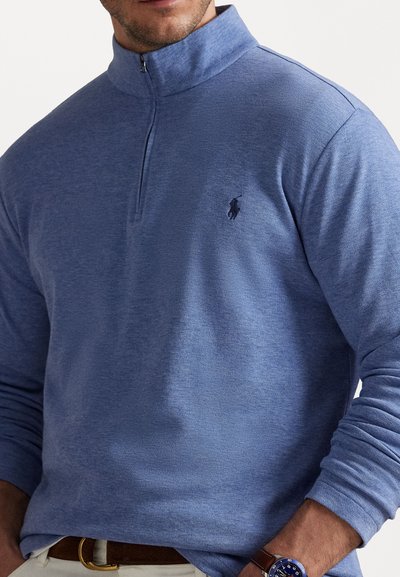 Sudadera de media cremallera en azul claro, hecha de un suave tejido texturizado. Presenta un pequeño logotipo bordado en el pecho y mangas largas.