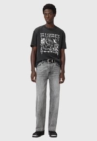 Camiseta gráfica negra con estampado blanco, combinada con jeans rectos grises. El conjunto incluye un cinturón negro y calzado negro con acentos blancos.