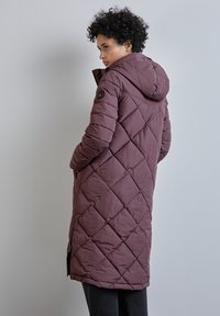 Lång vadderad pufferjacka i mauve, med huva, sidofickor och synliga sömnadsmönster. Slät textur med en avslappnad passform.