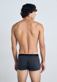 Dunkelgraue Boxershorts mit einem schwarzen elastischen Bund, enge Passform und glatter Textur, getragen von einer Person, die von hinten betrachtet wird.